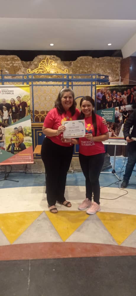 person writing in a notebook beside by an iPad, laptop, printed photos, spectacles, and a cup of coffee on a saucer
